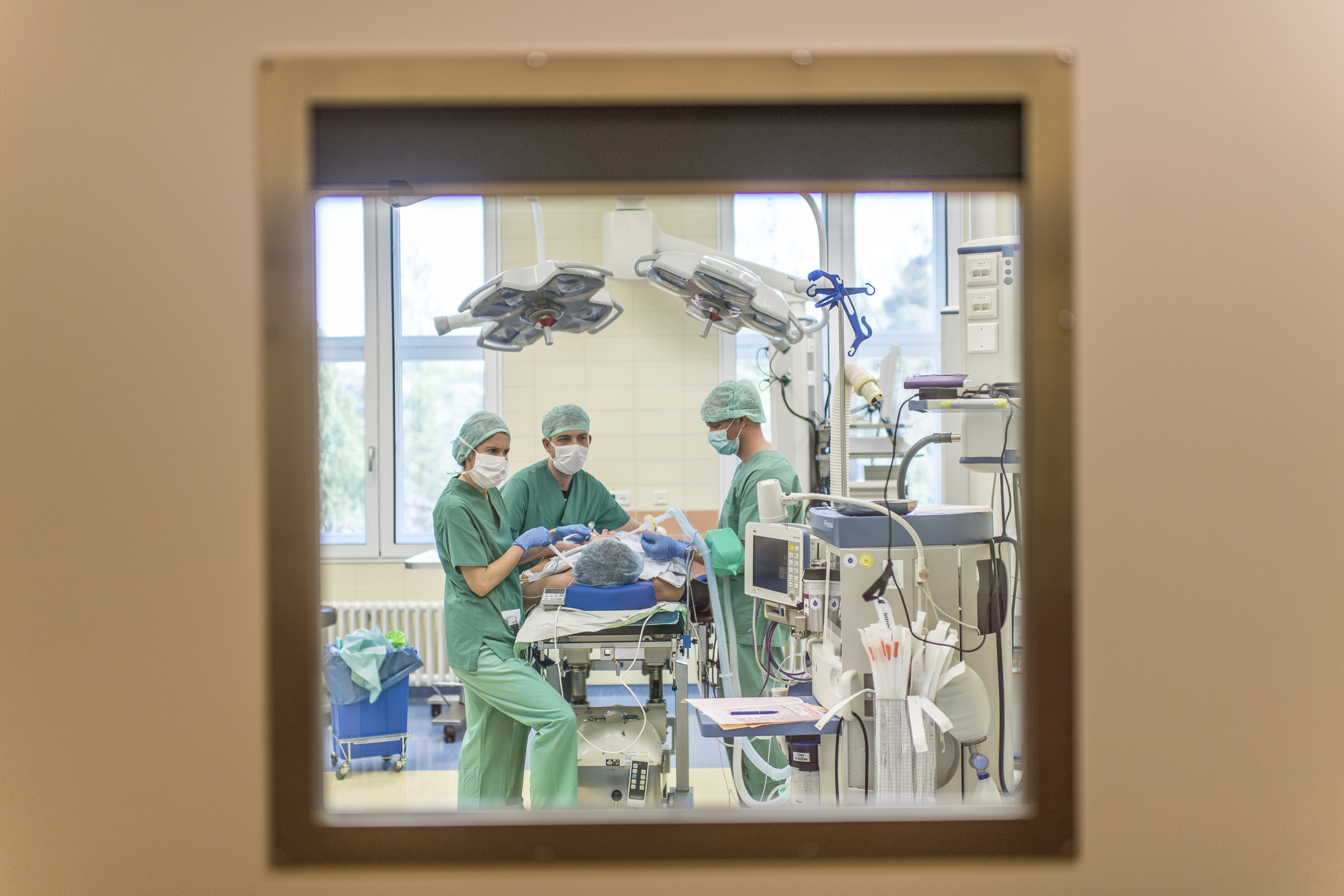 Blick durch ein Türfenster in einen Operationssaal. Medizinisches Personal operiert einen Menschen.