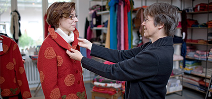 Verkäuferin hilft Kundin bei der Anprobe einer roten Wolljacke