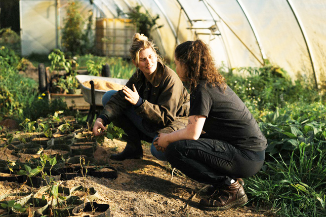Zwei Bio-Bäuerinnen hocken im Gewächshaus und führen ein Fachgespräch.