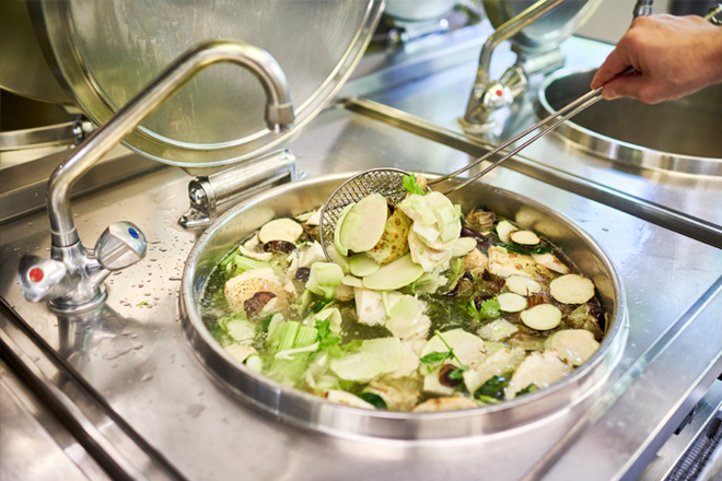 Hand rührt eine Gemüsesuppe in der Krankenhausküche.